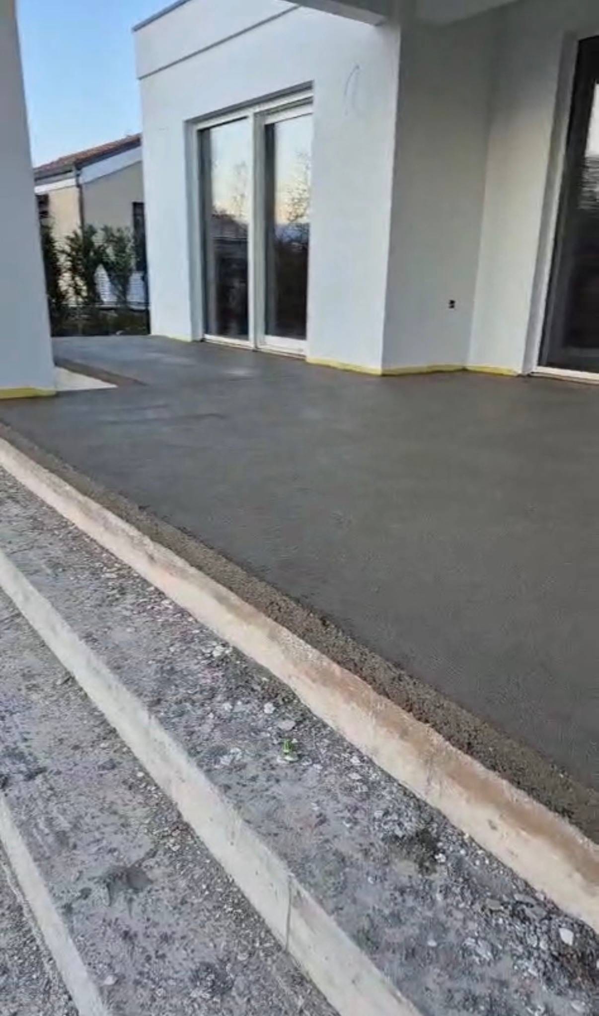 Bijela prizemnica s velikim staklenim stijenama, gotova siva terasa i žuta rubna traka uz zidove