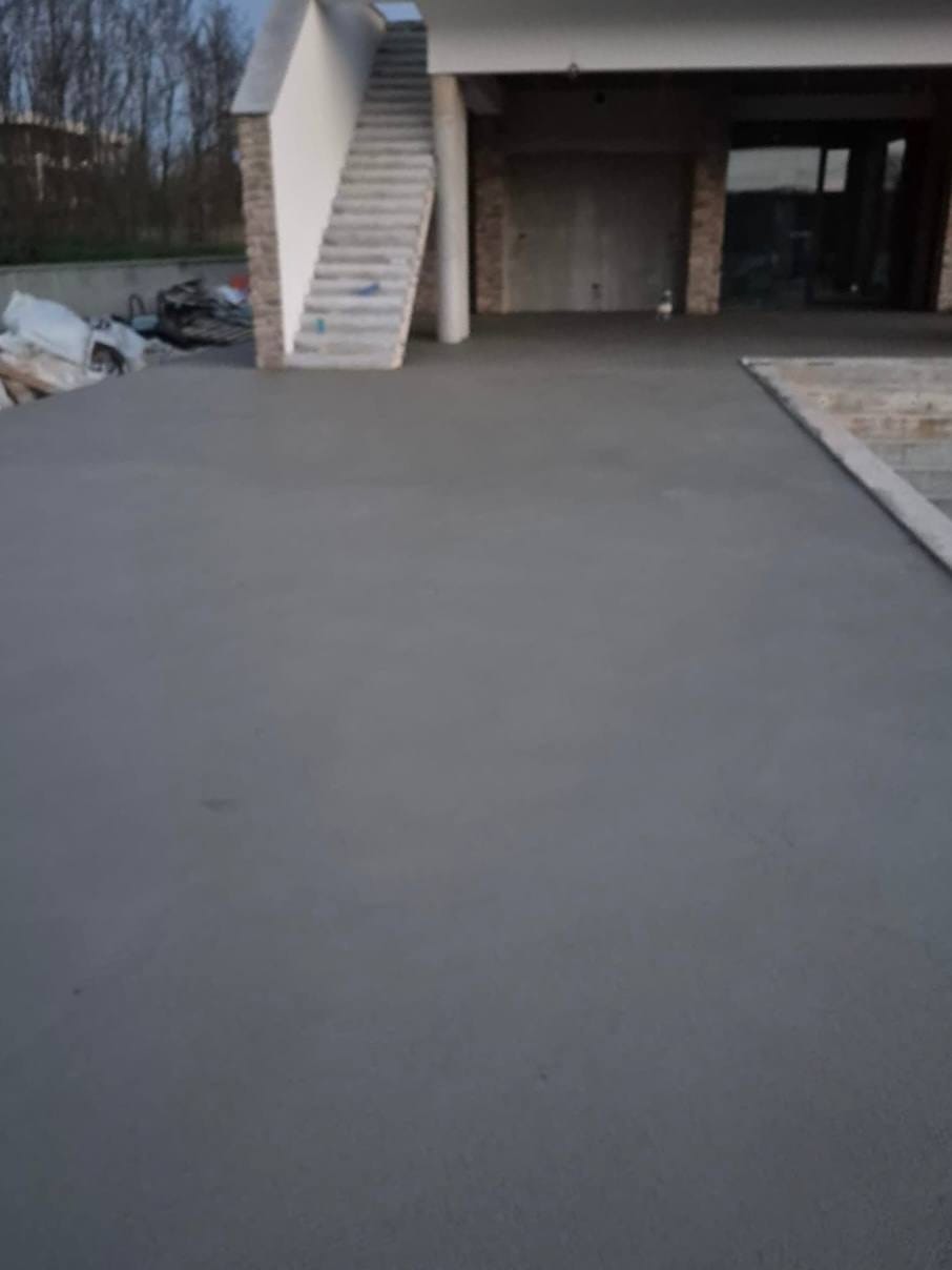 Velika gotova siva vanjska ploha ispred kuće u izgradnji, vanjsko stubište i kameni stupovi